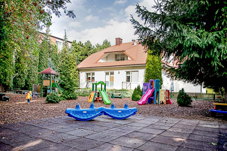 Plac zabaw na terenie przedszkola a za nim piękny budynek Owocowego Przedszkola.
